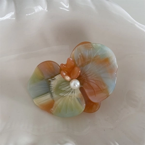 Detail of orchid acetate hair clip with pearl and bear center on a ceramic plate