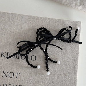Detail of elegant black beaded bow hair clip with white pearls on a soft linen background