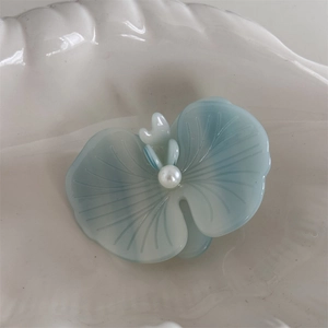Detailed macro view of light blue orchid hair clip with pearl center on ceramic plate