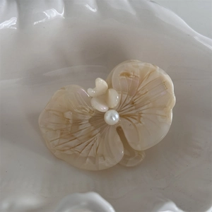 Close-up of cream acetate flower hair clip with pearl center on ceramic plate