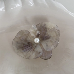 Detail of orchid-shaped acetate hair clip with marble texture and center pearl