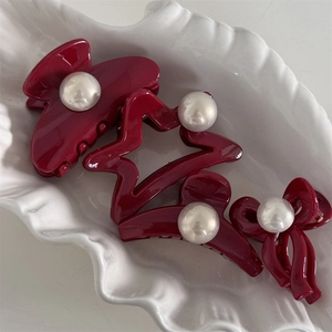 Set of four burgundy hair clips with pearls on a white ceramic display tray