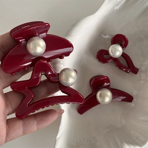 Close-up of four red resin hair clips with elegant pearl accents on a shell plate