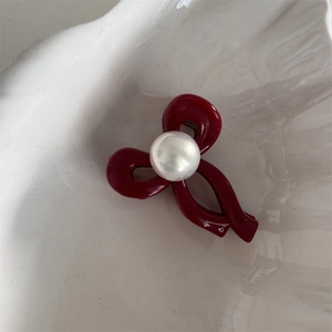 Close-up of burgundy twisted ribbon hair claw clip with a large pearl in a shell dish