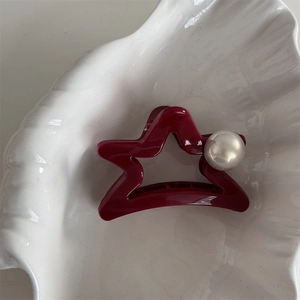 Detail showing red star hair claw clip with large pearl on textured decorative tray
