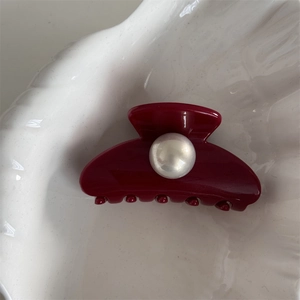 Close-up of deep red resin hair claw clip with glossy finish and central faux pearl detail
