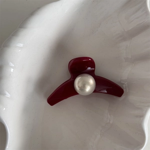 Close-up of a red hair claw clip with a large pearl detail on a white shell tray