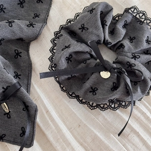 Grey lace scrunchie with black bow pattern and golden heart charm on soft fabric