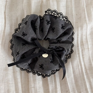 Detail of dark grey scrunchie with black lace trim and golden bow pendant charm