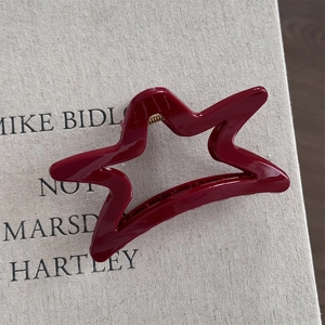 Macro shot of red star hair claw with golden metal spring on beige fabric