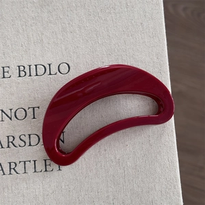 Close-up of a minimalist burgundy crescent hair claw clip with a glossy mirror finish texture