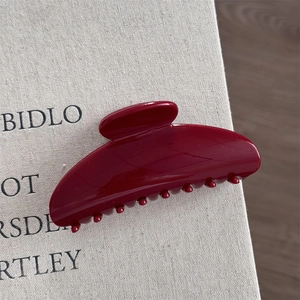 Close-up of a glossy dark red resin hair claw clip resting on a textured fabric book cover