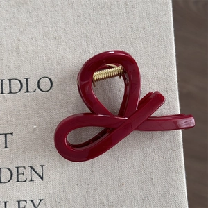 Detailed view of the dark red cross-knot hair claw clip with a glossy finish and gold spring