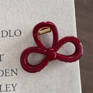 Close-up of deep red bow hair claw with gold spring detail on linen background