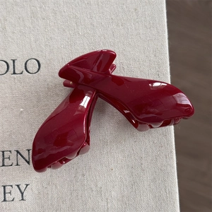 Detailed view of glossy burgundy red hair claw clip with high-shine finish on fabric