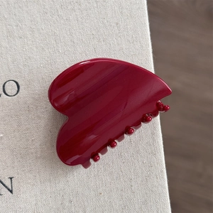 Macro detail of glossy dark red resin hair claw clip with non-slip teeth on white fabric