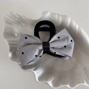 Détail d'un chouchou nœud en tissu gris à pois sur une coupelle décorative blanche