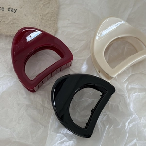 Close-up of three glossy D-shaped hair claws in wine red, cream white, and black colors