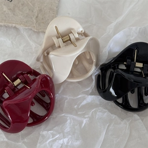 Three glossy triangle hair claws in burgundy, cream, and black on white tissue paper