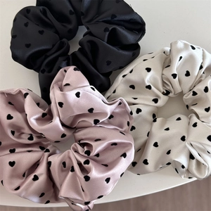 Detailed view of satin scrunchies in black, pink and cream with velvet heart patterns
