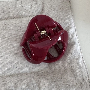 Close-up of deep red glossy hair claw clip with golden metal spring on linen background