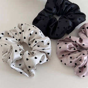 Detailed view of satin heart-print scrunchies in ivory, black, and dusky pink colors