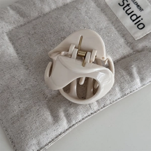Close-up of cream-colored resin shark hair claw clip with golden metal spring