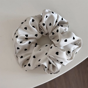 Detail view of smooth white satin scrunchie featuring elegant black heart patterns