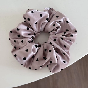 Close-up of pink satin scrunchie with black heart pattern and silky texture