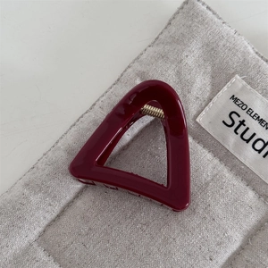 Macro shot of triangular burgundy resin hair claw with a metallic spring on quilted fabric
