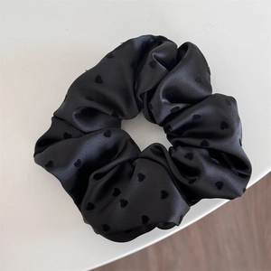 Detailed shot of black satin scrunchie featuring elegant small heart patterns
