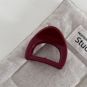 Detailed view of glossy burgundy triangular hair claw on textured linen fabric