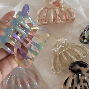 Detail of hand holding a sea shell acetate claw clip with strong metal spring