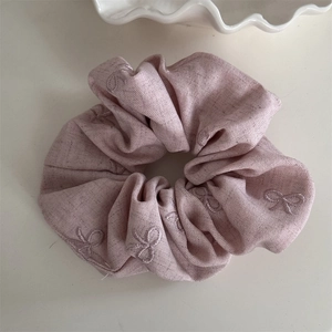 Détail d'un chouchou rose en tissu avec des nœuds brodés et une texture douce élégante