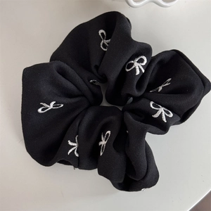 Détail du chouchou en maille noire avec motifs de nœuds blancs brodés et texture douce