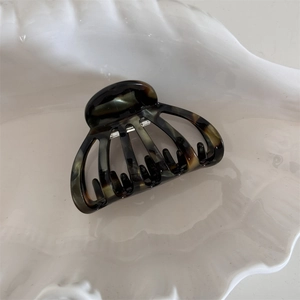 Detail of shell-shaped acetate hair claw clip with tortoiseshell texture on white tray