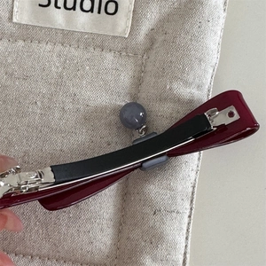 Détail d'une barrette à cheveux bordeaux brillante avec un pendentif à perle grise mate