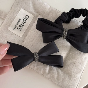Détail de barrettes nœuds en satin noir avec centre en strass brillants sur fond de lin