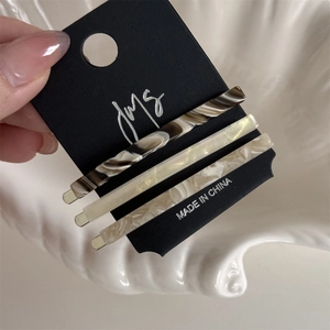 Three acetate hair clips in tortoise shell and cream patterns on a black display card