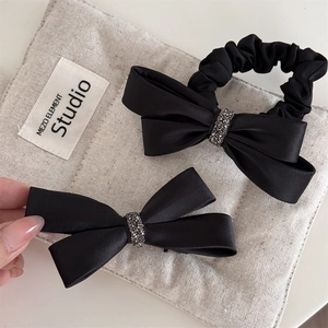 Détail de l'ensemble de nœuds en satin noir avec strass sur une pochette en lin