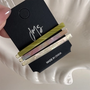 Close-up of three acetate hair clips in olive green, marble pink-blue, and pearl white