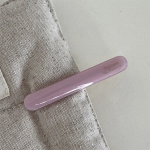 Close-up of purple acetate hair clip featuring gold lettering on cream canvas