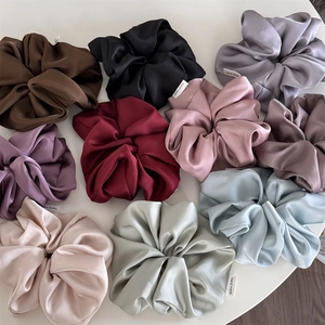 Close-up of premium satin hair scrunchies in various colors with handmade woven labels