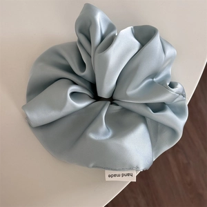 Detail of light blue satin oversized scrunchie with handmade label and silky texture