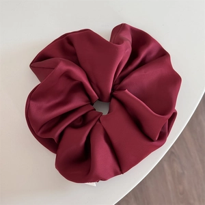 Detailed view of large burgundy satin scrunchie showing glossy fabric texture and pleats