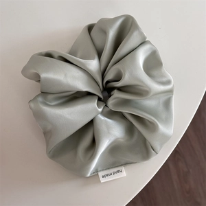 Detail of sage green satin oversized scrunchie featuring white handmade textile label