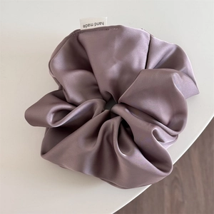 Close-up of a large satin scrunchie in purple with a handmade label on a white surface