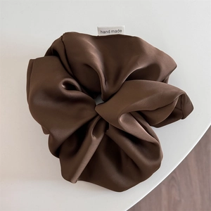 Detailed macro view of dark coffee satin scrunchie featuring handmade woven label