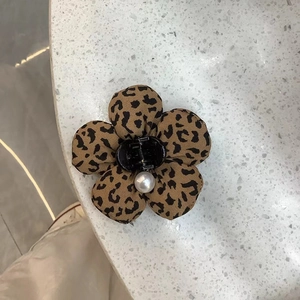 Detail view of a leopard print fabric flower hair clip with a central faux pearl accent