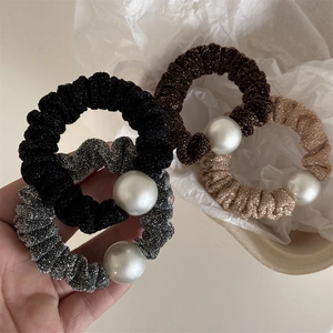 Close-up of four glitter fabric hair scrunchies with large pearl beads in neutral colors